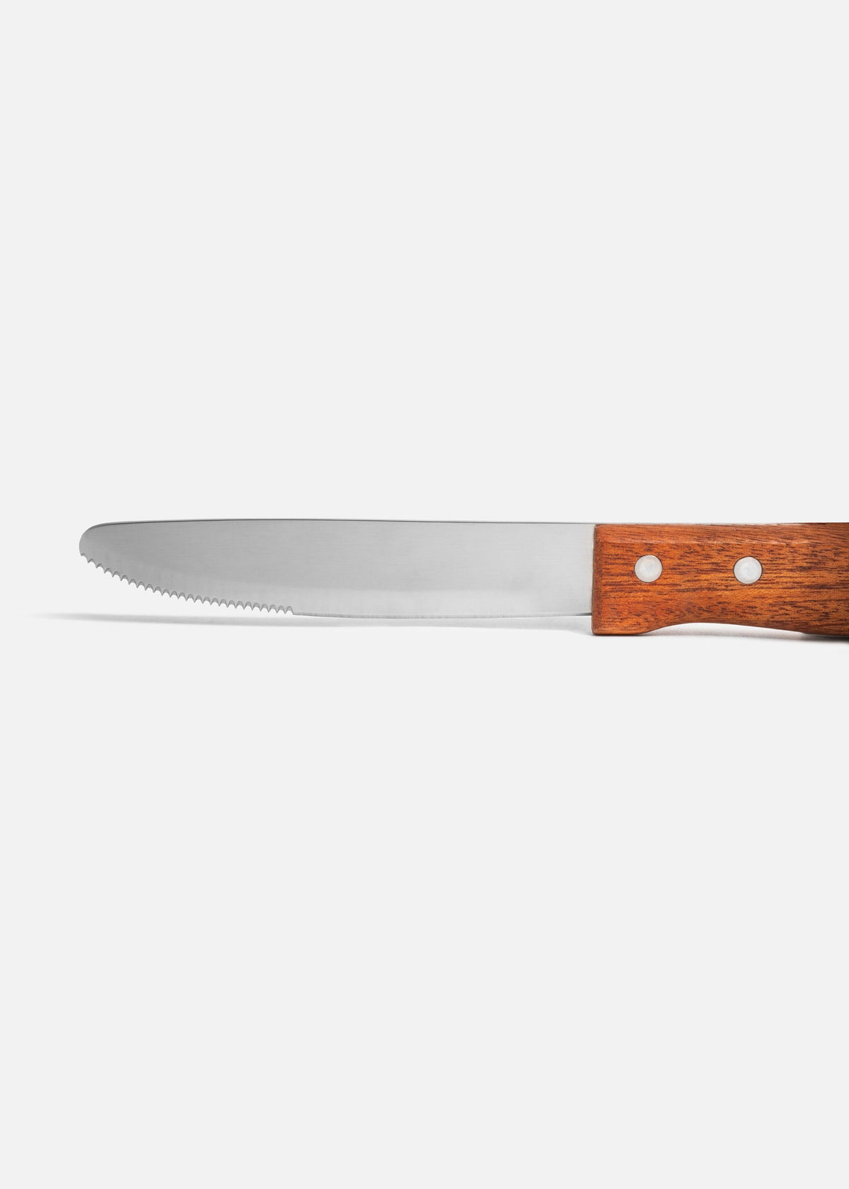 Detalle de la hoja de punta redonda, borde serrado y mango de madera remachado del cuchillo de mesa.