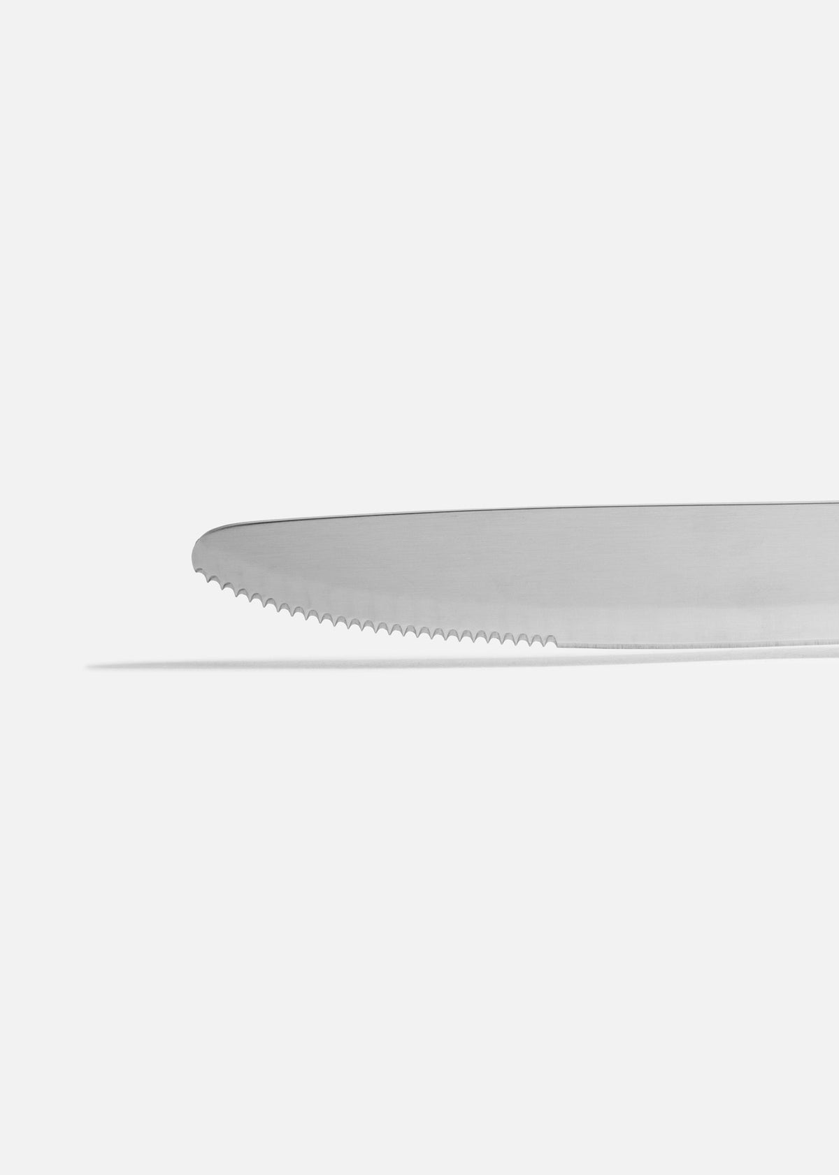 Acercamiento del borde serrado y la punta redonda de la hoja de acero inoxidable del cuchillo para carne.
