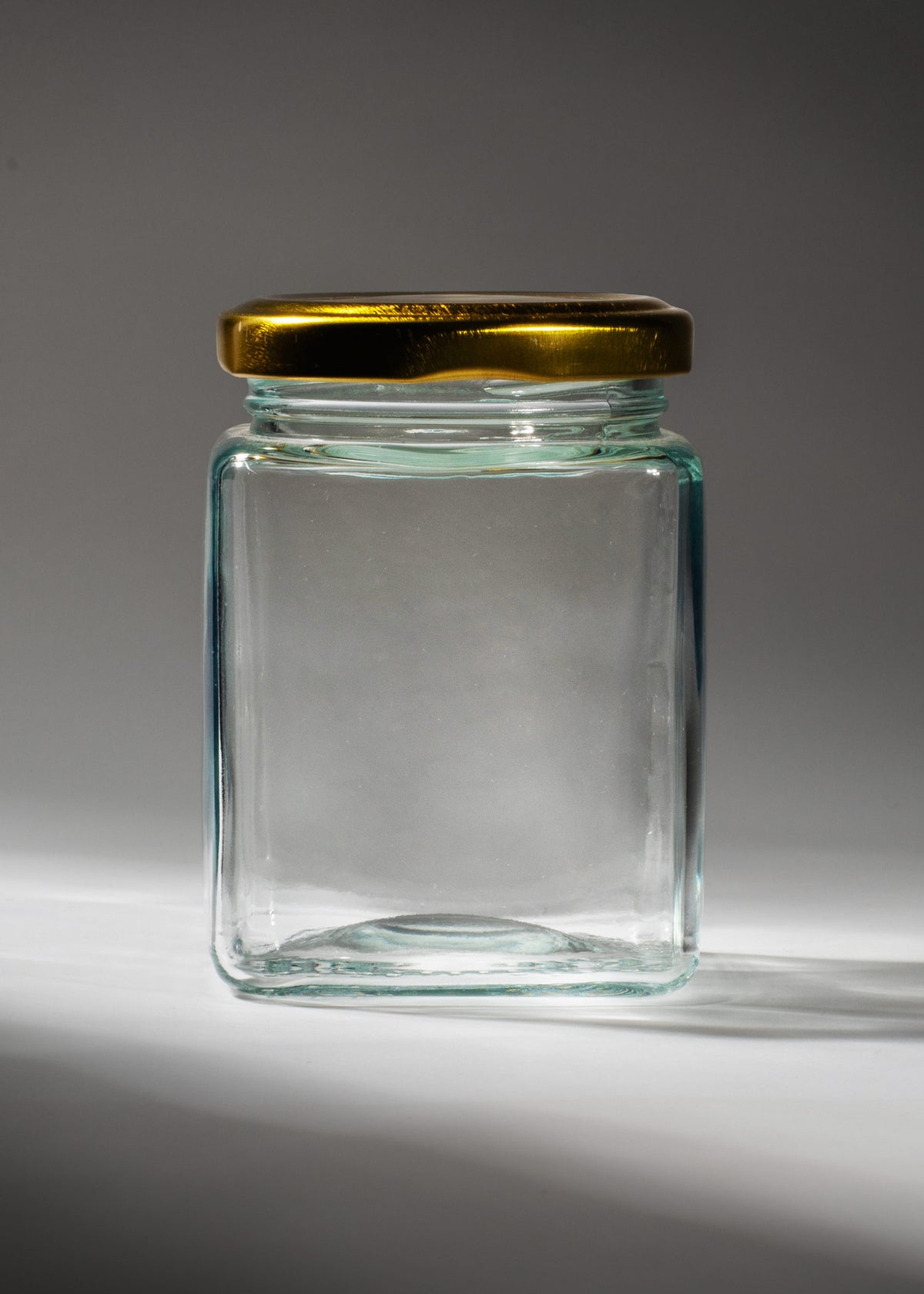 Frasco cuadrado de vidrio transparente de 200 ml con tapa de rosca dorada, vista completa.