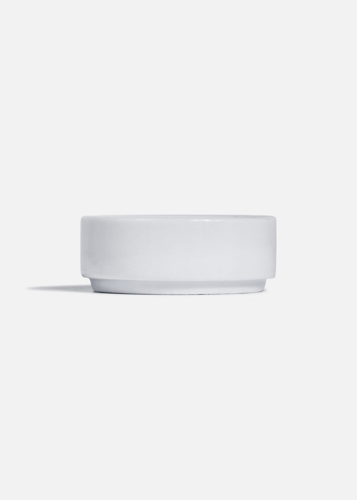 Vista lateral de platito hondo de porcelana blanca con borde elevado.