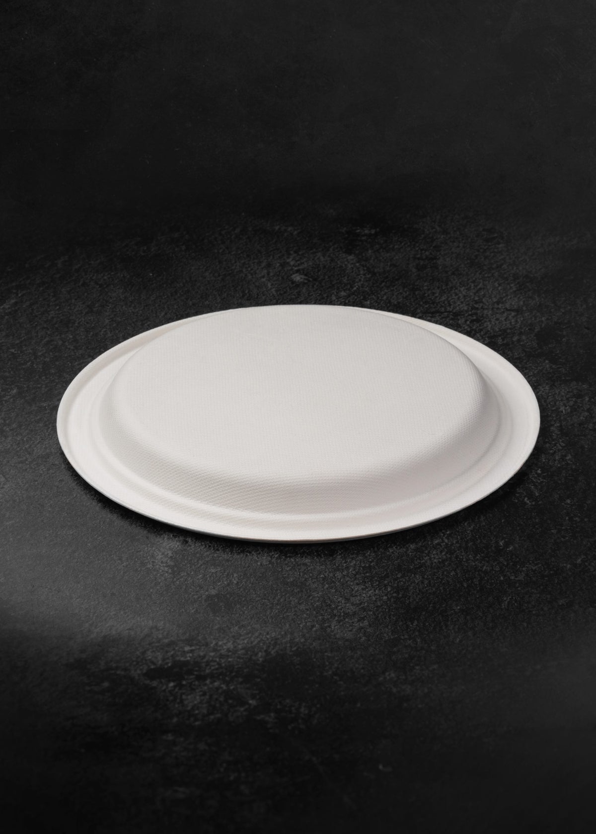 Vista inferior en ángulo del plato compostable blanco redondo de 22.7 cm.