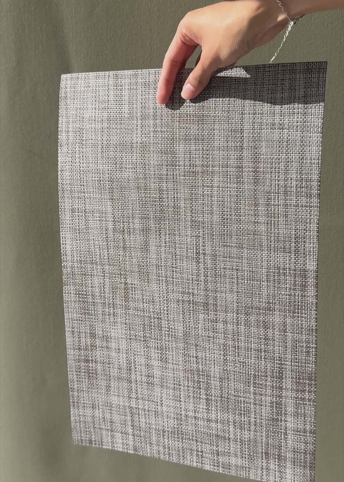 Cargar vídeo: Video en luz natural del mantel individual beige jaspeado que muestra la textura y flexibilidad del tejido.