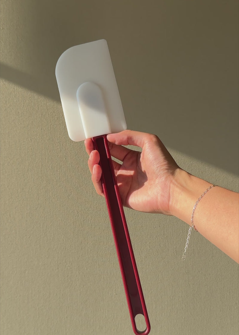Espátula miserable de silicón blanco con mango rojo de 35.5 cm mostrada con luz natural.