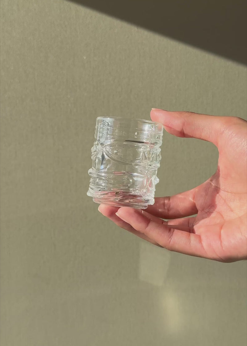 Video en luz natural del tequilero Tiki de 60 ml que muestra su rostro en relieve y vidrio brillante.